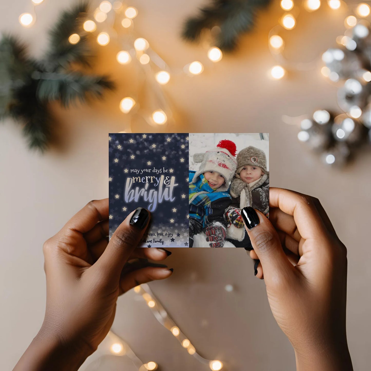 Woman holding navy christmas photo card with string lights in background