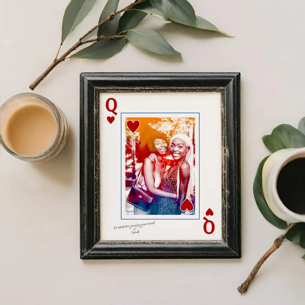 Queen of hearts portrait in distressed black frame  next to a beige coloured candle and green leaves