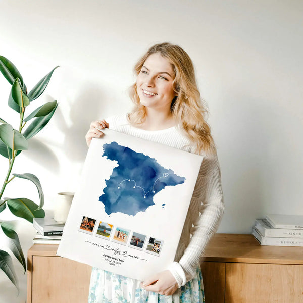 Smiling woman with blond hair holding a print of Spain map keepsake collage. She stands in front of a wooden bureau.