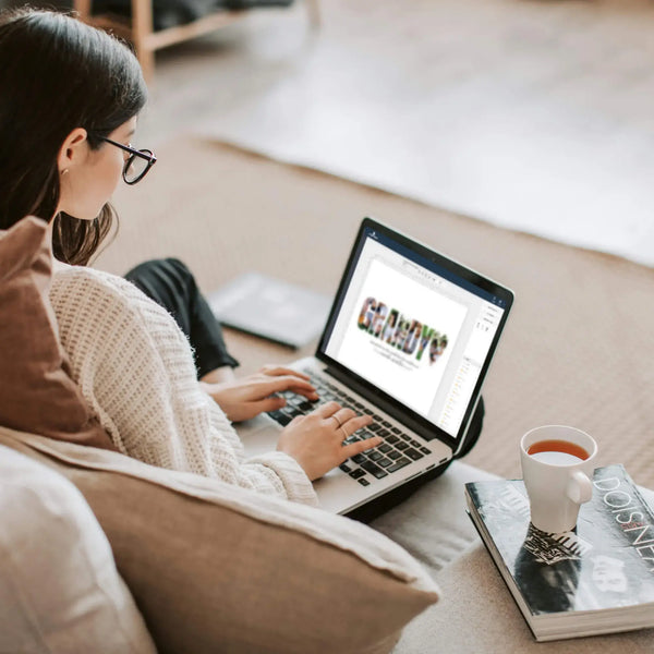 Woman editing grandy photo collage template on laptop while sitting on couch next to a cup of tea.