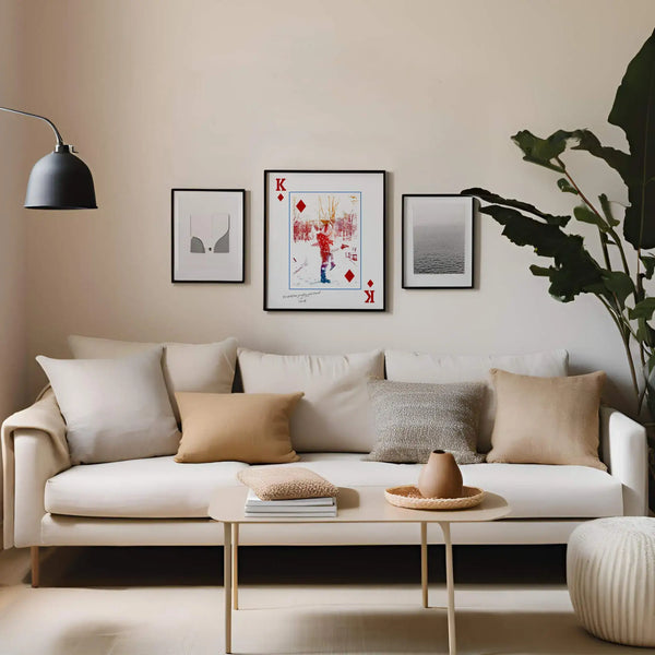 King of Diamonds Style Portrait in sleek black frame hanging on cream coloured living room wall between two other art frames. Below is an ivory coloured couch with several comfy pillows.