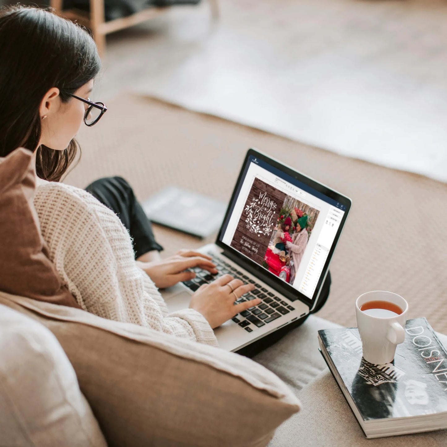 Woman editing holiday photo card template on laptop next to a cup of tea